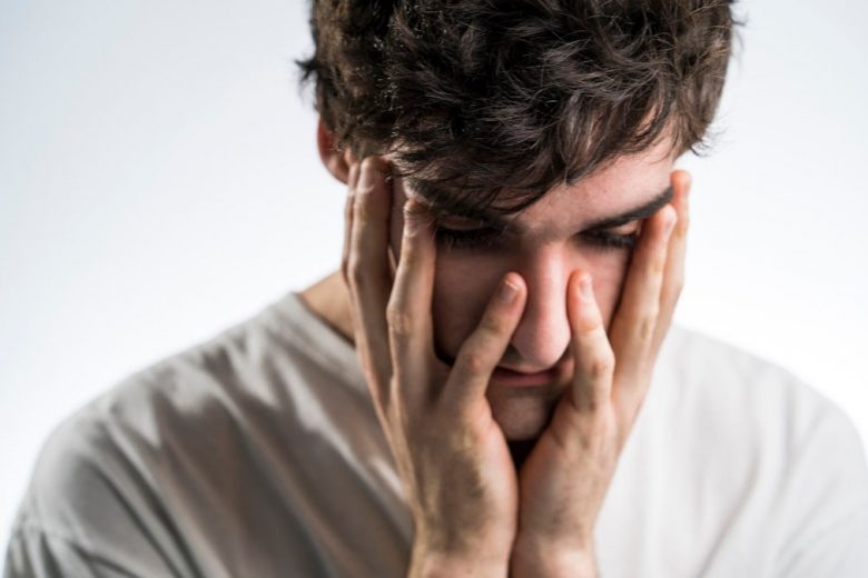 Sad man holding face with white shirt and black hair